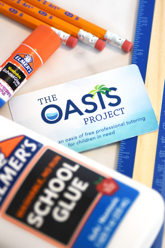 Close up photo of an arrangement of glue stick, Oasis business card, Elmer's School Glue bottle, and pencils